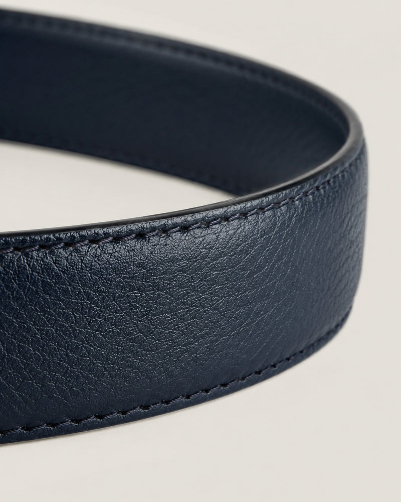Macro photograph of the pebbled full-grain surface and stitched edge of a navy Harrow belt